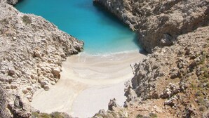 A rocky coastal landscape with a clear blue sea and a sandy beach.