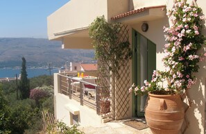 A balcony with a view of the sea, a potted plant, and a door with a green shutter. - The Garden of Zephyrus (Chania)