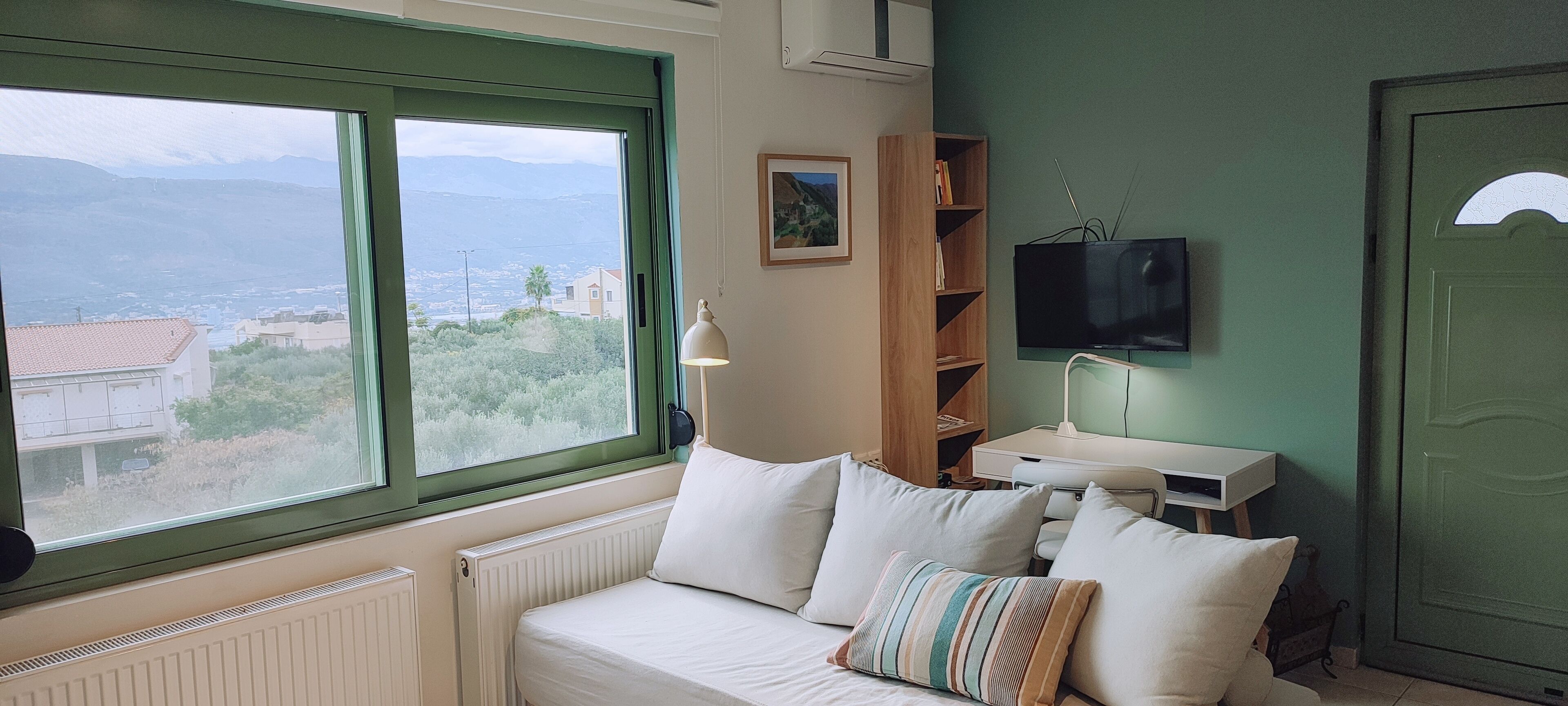 Una habitación con cama, televisor, estantería y vistas a la montaña.