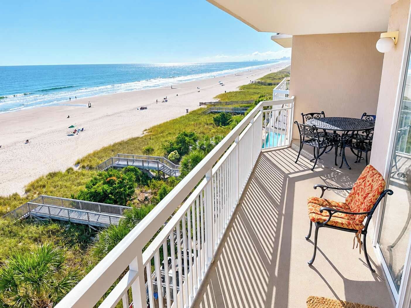 A balcony with a view of a beach, outdoor furniture, and a pool.