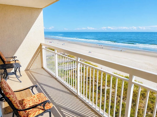 A balcony with a view of a beach, a chair, and a table.