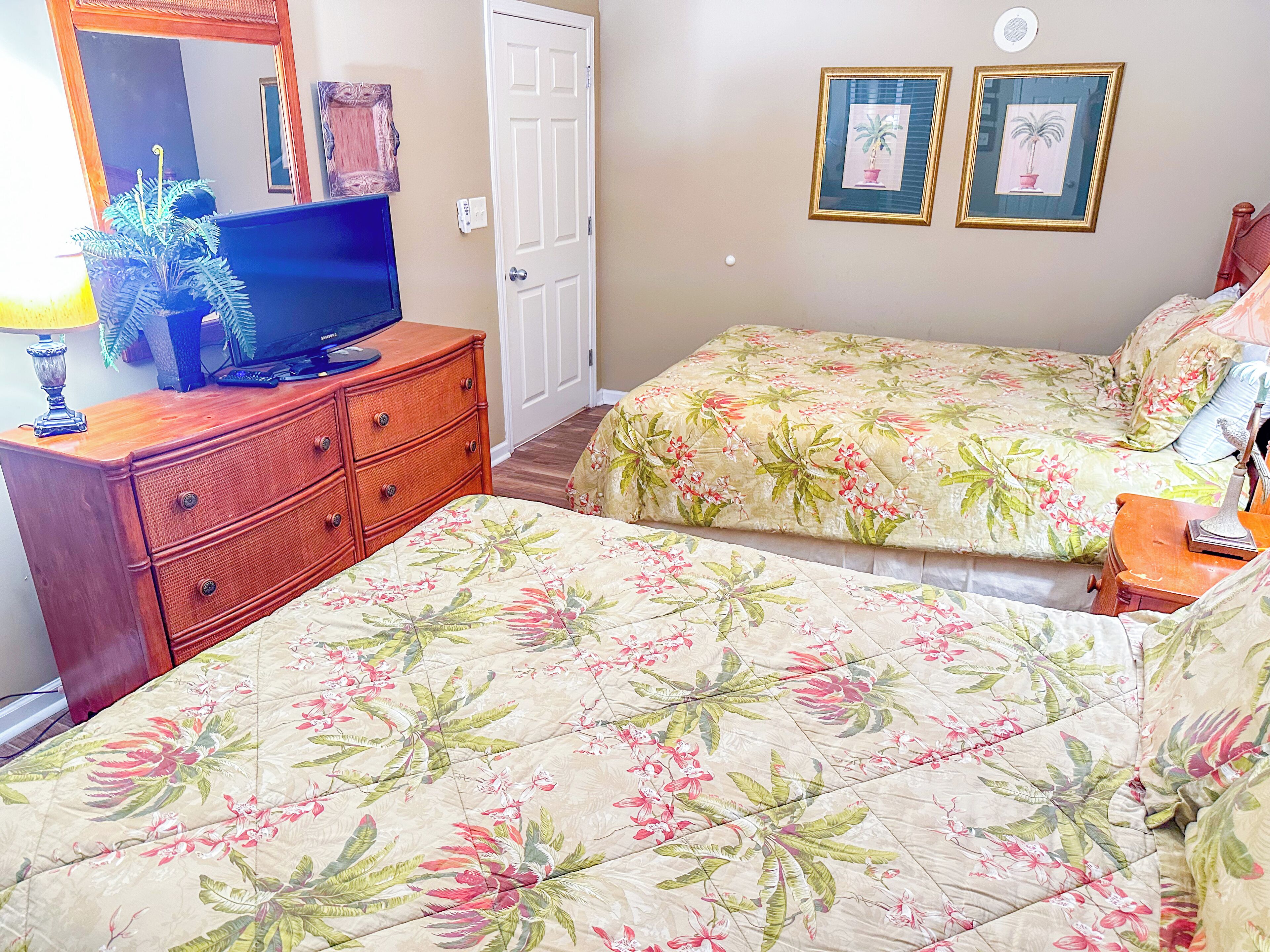 A bedroom with a bed, a dresser, a television, and two framed pictures on the wall.
