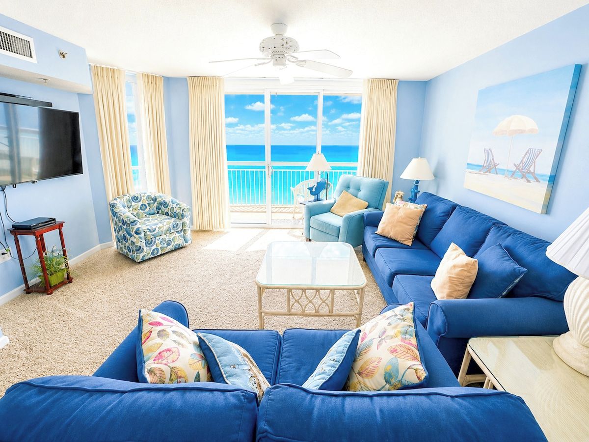 A living room with a large blue sofa, a television, and a view of the ocean.