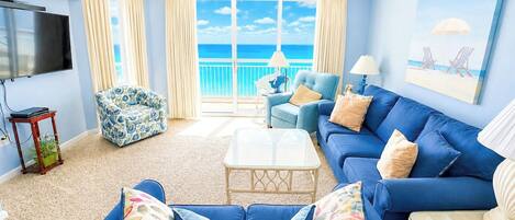 A living room with a large blue sofa, a television, and a view of the ocean.