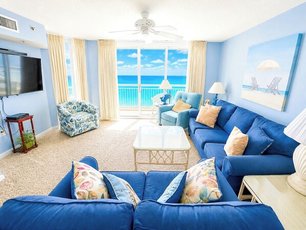 A living room with a large blue sofa, a television, and a view of the ocean.