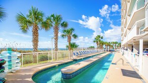 A pool area with clear blue water, palm trees, and a white fence. - Crescent Shores S 1309 - Oceanfront Luxury & Unmatched Views! (North Myrtle Beach)