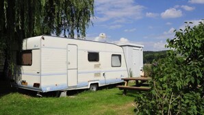 Una caravana blanca con puerta lateral y ventana pequeña, estacionada sobre césped con una mesa de picnic cerca.