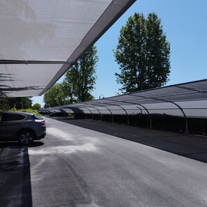 Un espace de stationnement avec une voiture à l’abri sous une grande structure en forme de tonnelle.