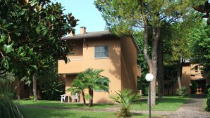 A two-story building with a brown facade, a paved pathway, and surrounding greenery. -  TWO-ROOM APARTMENT SURROUNDED BY GREEN IN A QUIET RESIDENCE WITH POOL (Sirmione)