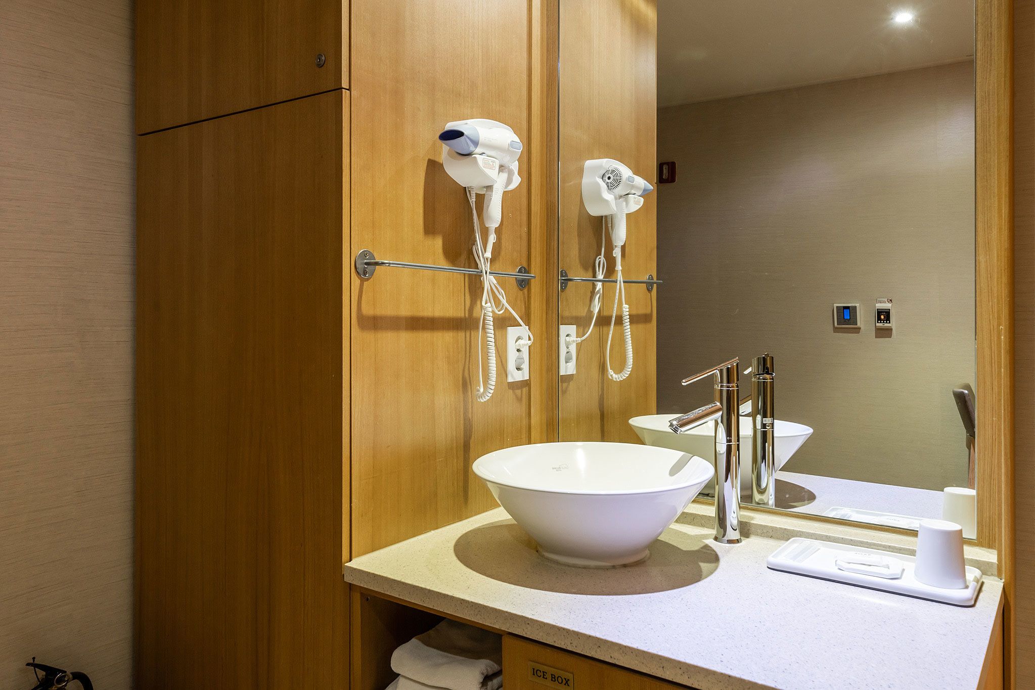 Un baño con tocador de madera, lavamanos blanco, espejo y dos secadores de pelo montados en la pared.