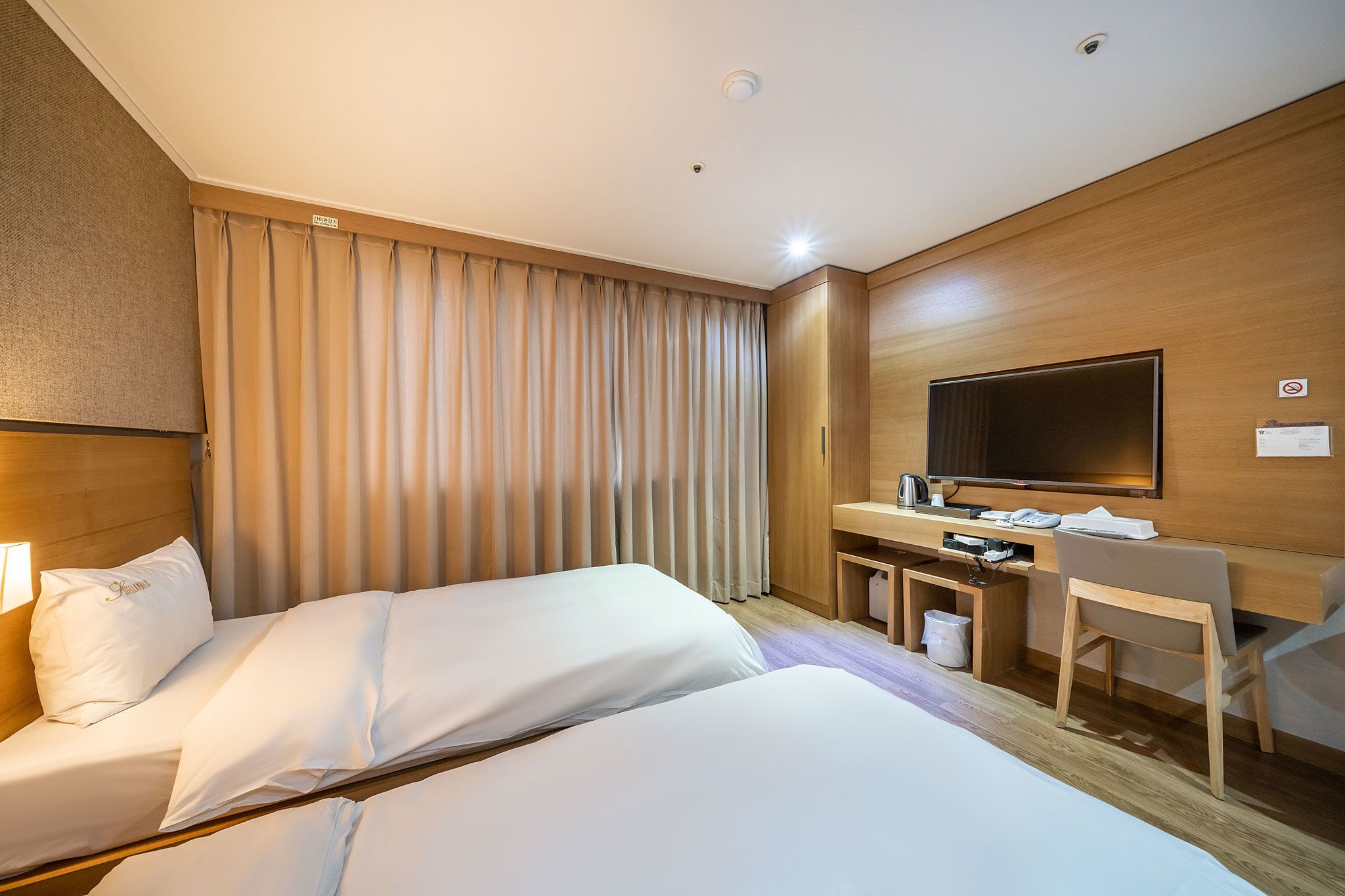 A hotel room with a bed, a desk, a chair, a television, and a window with curtains.