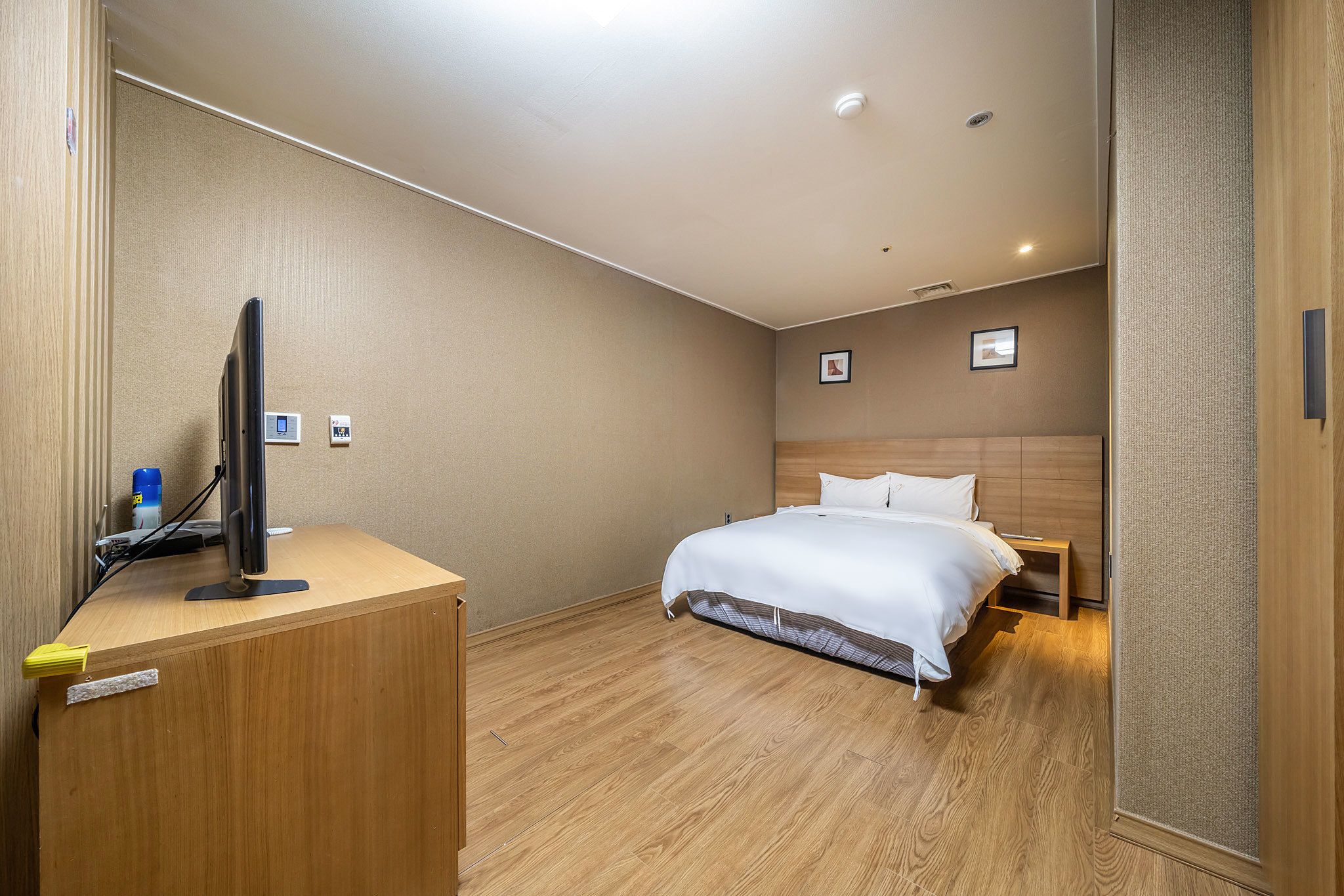 A hotel room with a wooden desk, a bed with white bedding, and a headboard.