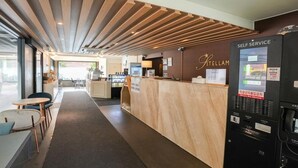 Een hotel receptie met een houten receptiebalie, een zelfbedieningsautomaat en een zithoek met tafels en stoelen.