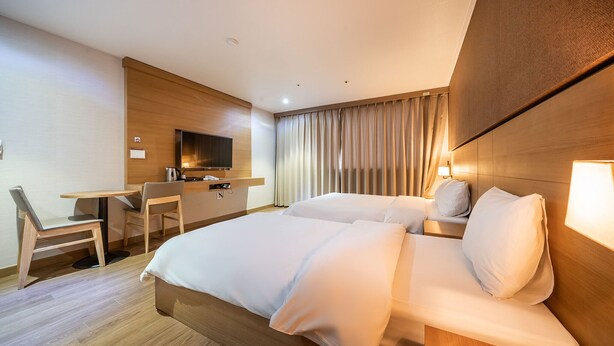 Een hotelkamer met een bed, een bureau, een stoel, een televisie en een gordijn.