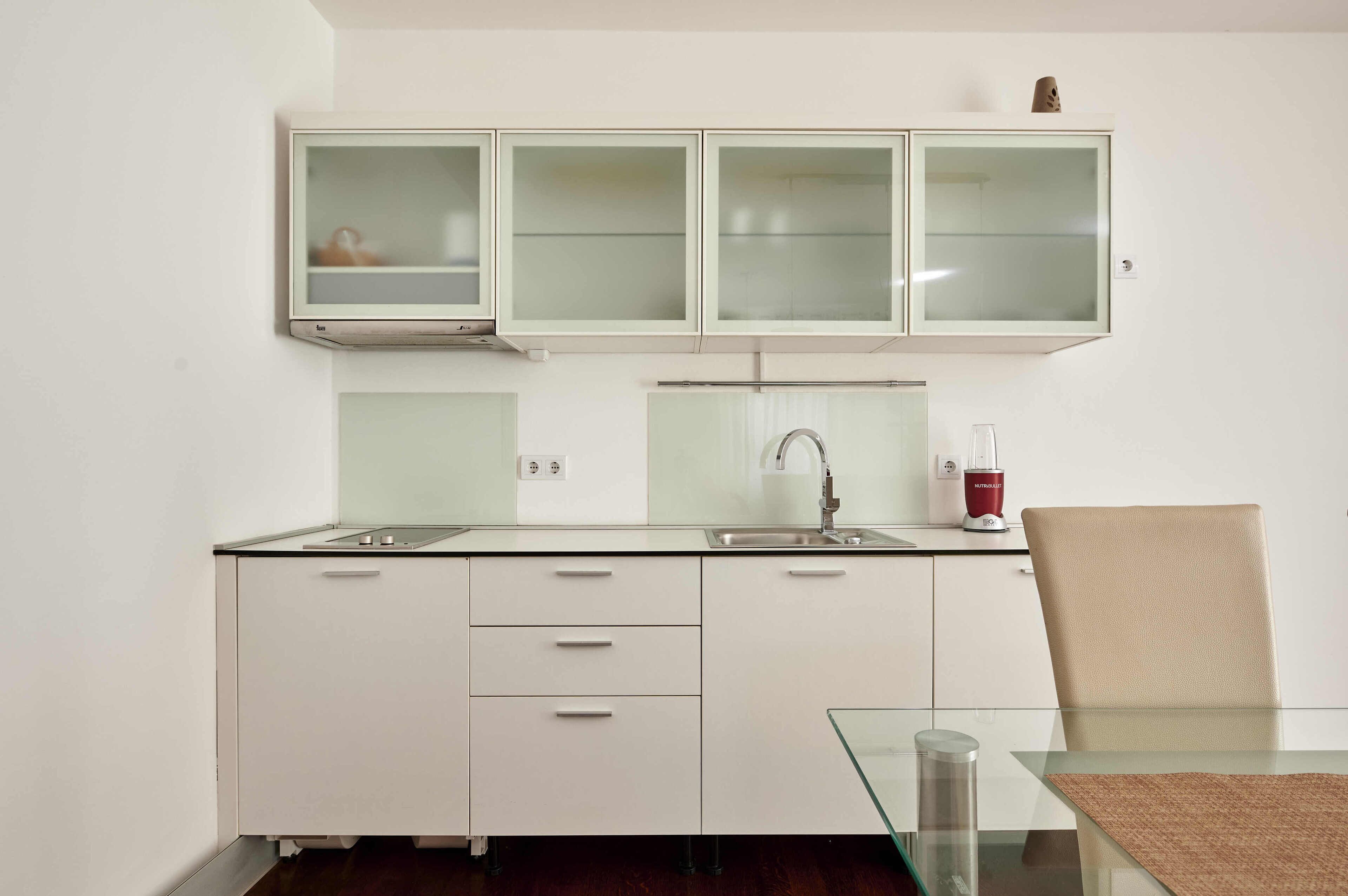 A modern kitchen with white cabinets, a glass-top dining table, and a red coffee machine.