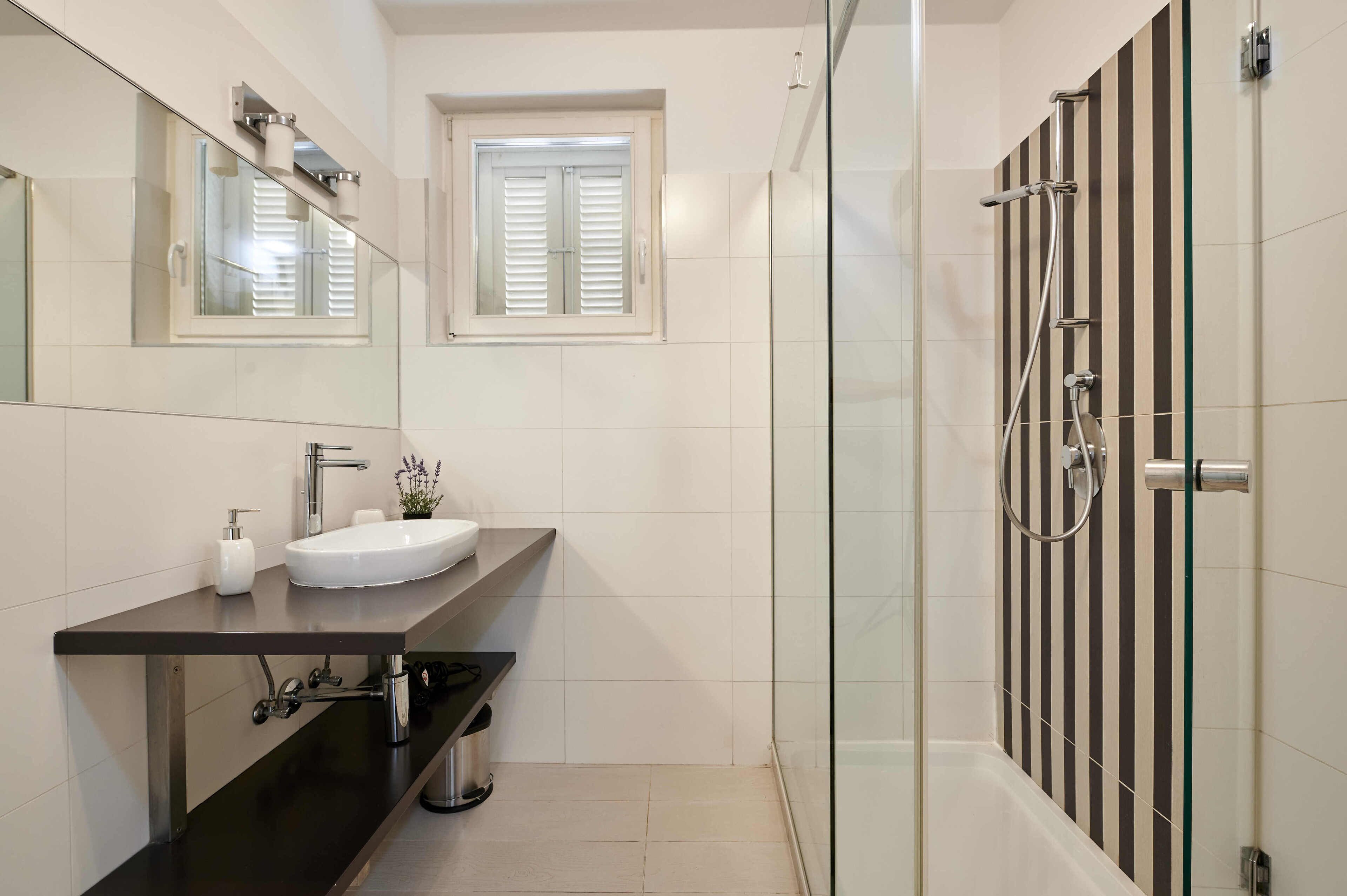 A modern bathroom with a glass-enclosed shower, a white sink, and a large mirror.