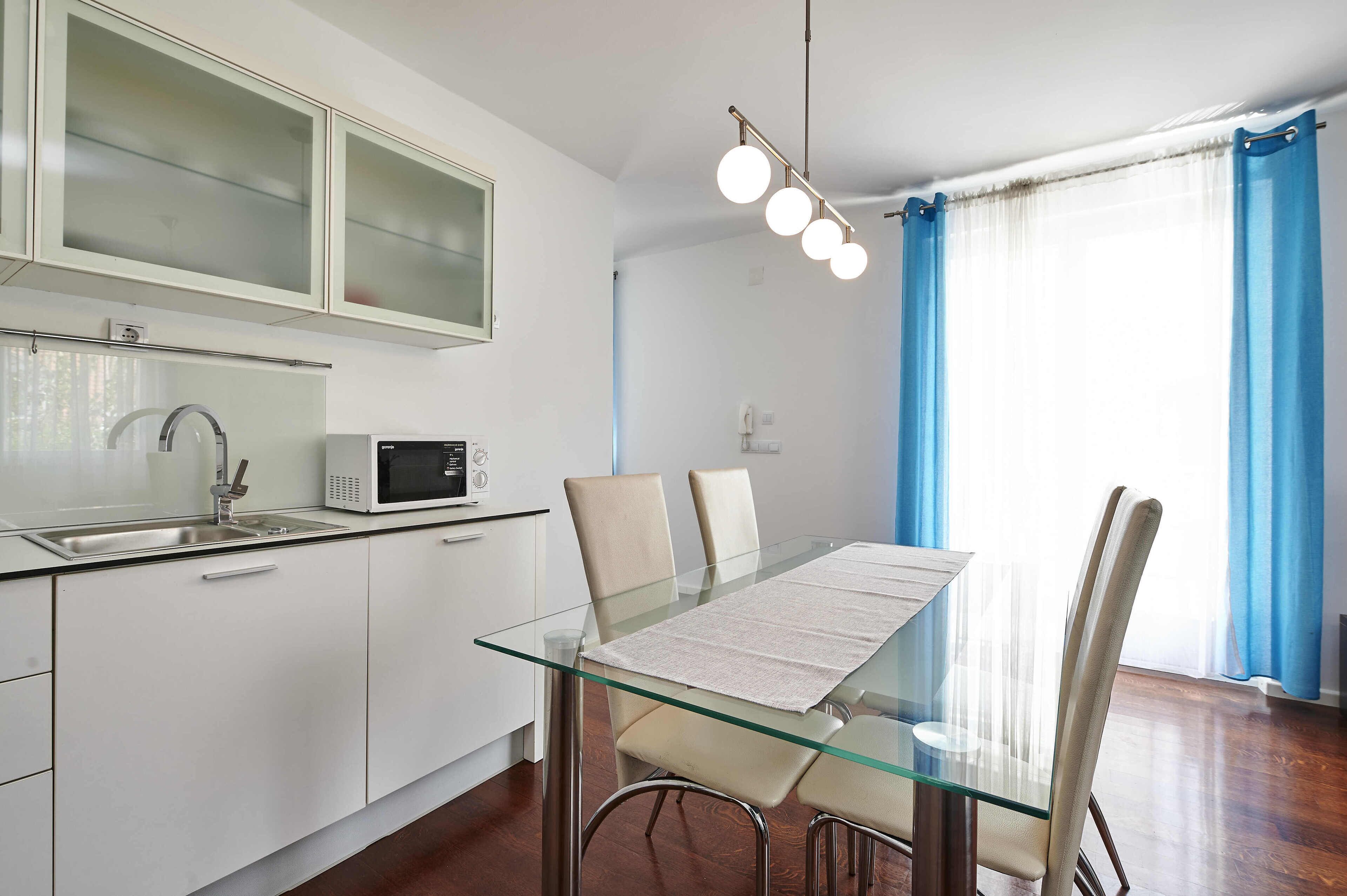 A modern kitchen with a microwave, a glass-top dining table, and a sink.