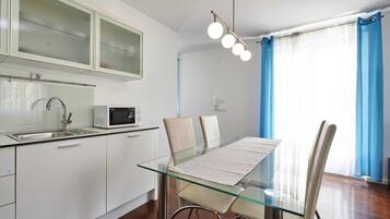 A modern kitchen with a microwave, a glass-top dining table, and a sink.