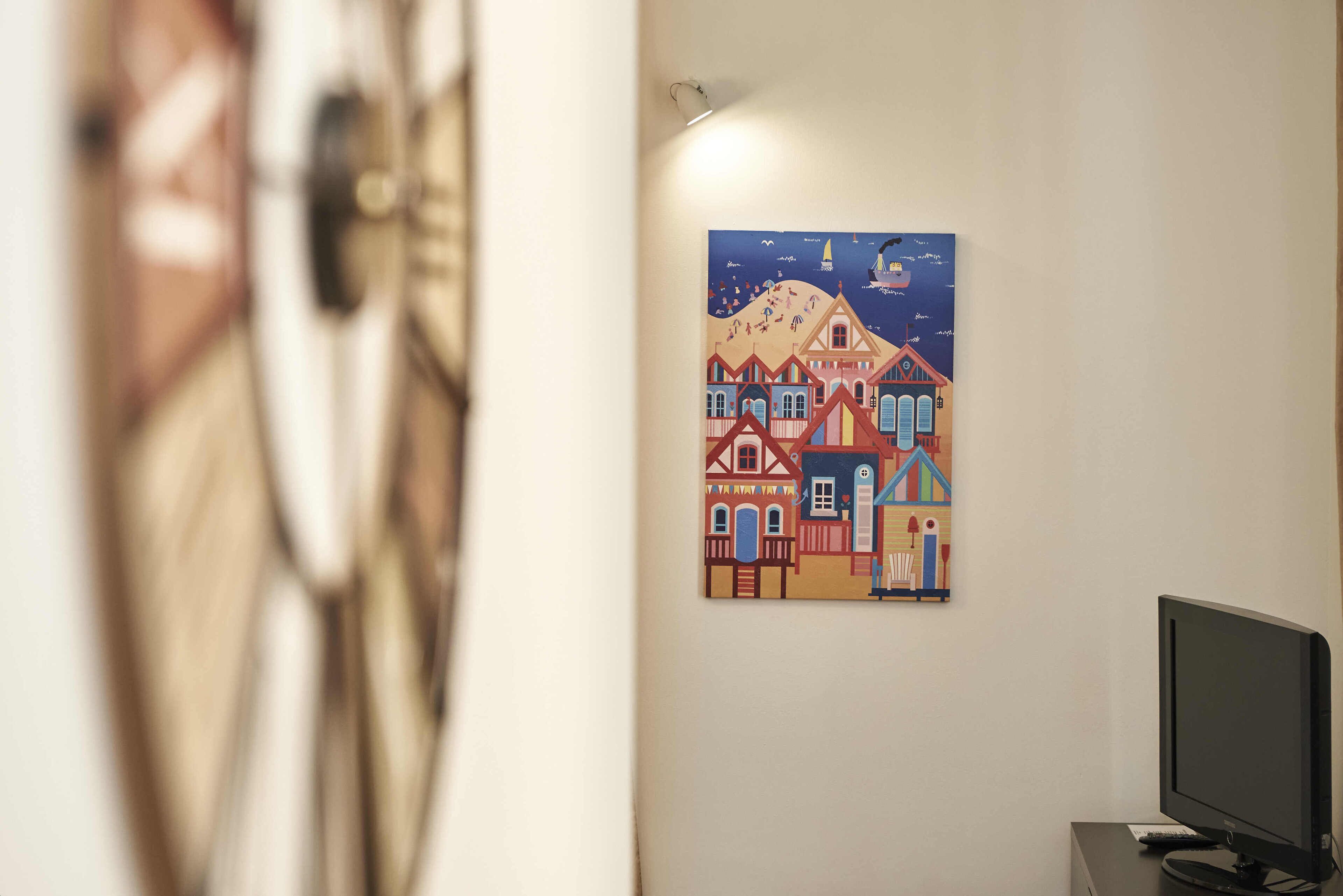 A room with a wall-mounted painting of a colorful mountain scene and houses, a television on a stand, and a door with a handle.