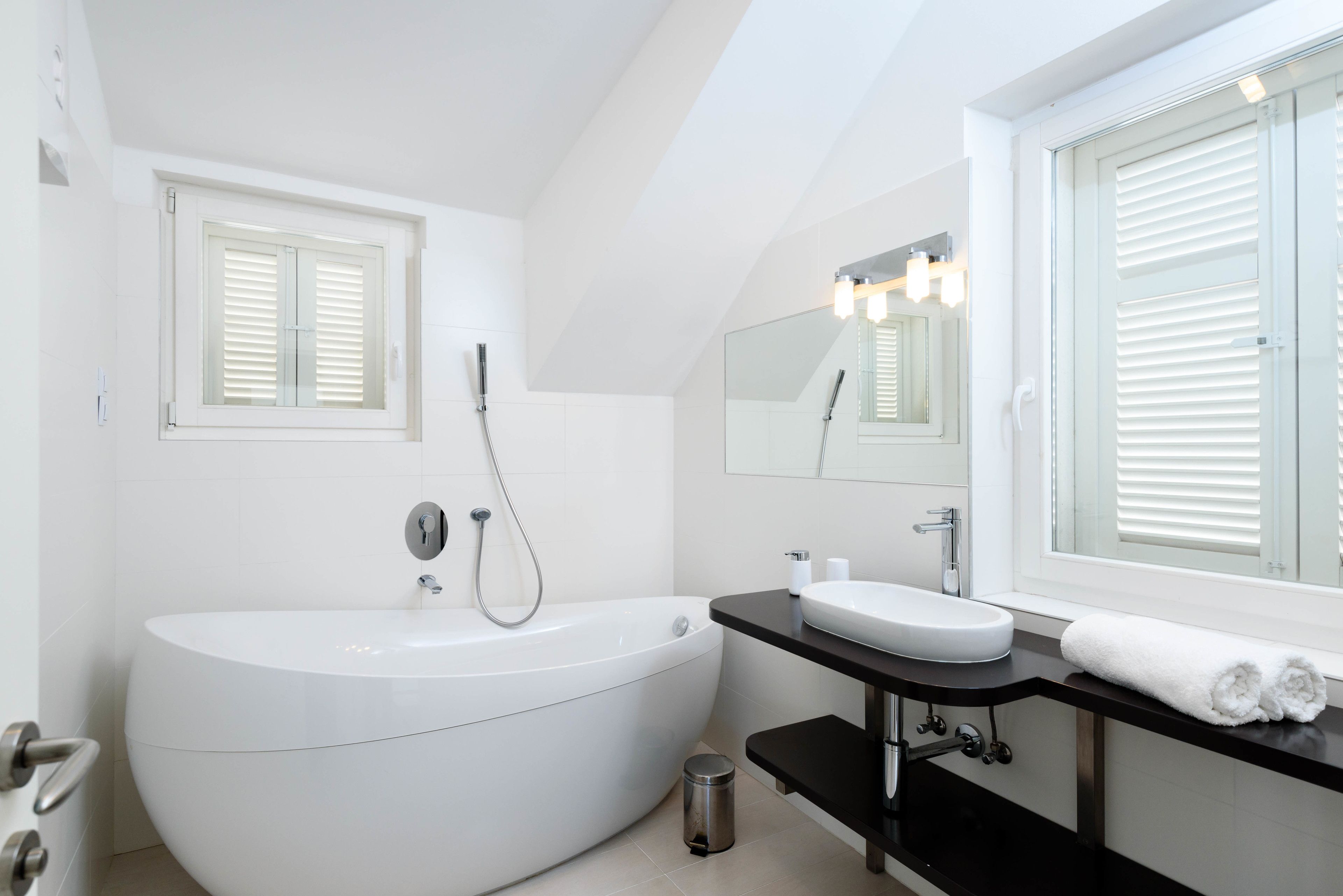 Une salle de bain moderne avec une baignoire sur pieds, un meuble-lavabo avec un miroir et une fenêtre équipée de stores.