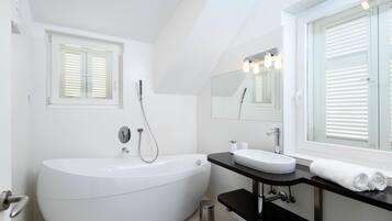 Une salle de bain moderne avec une baignoire sur pieds, un meuble-lavabo avec un miroir et une fenêtre équipée de stores.