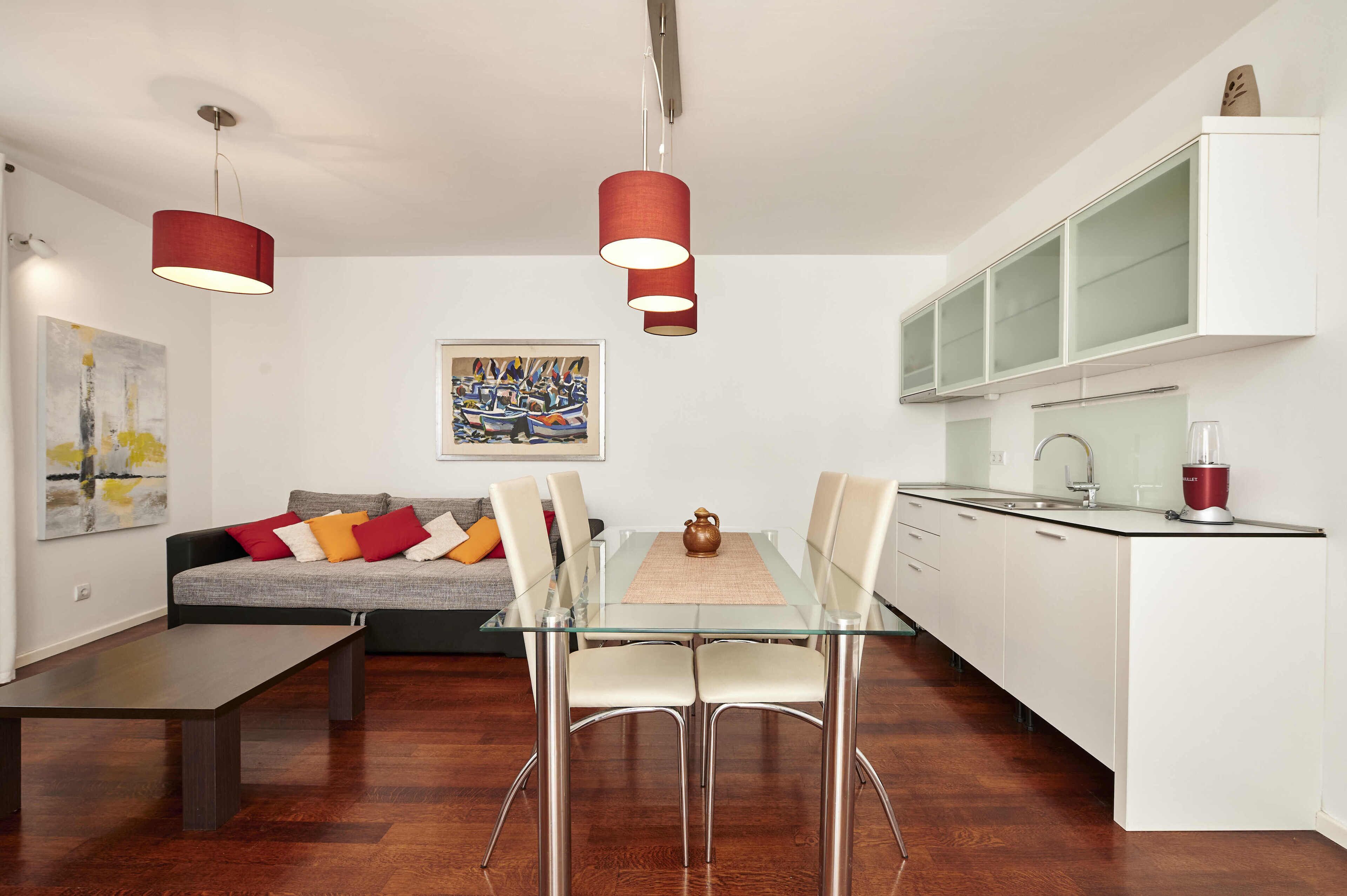 Une cuisine moderne avec des meubles blancs, une table à manger en verre et des suspensions rouges.