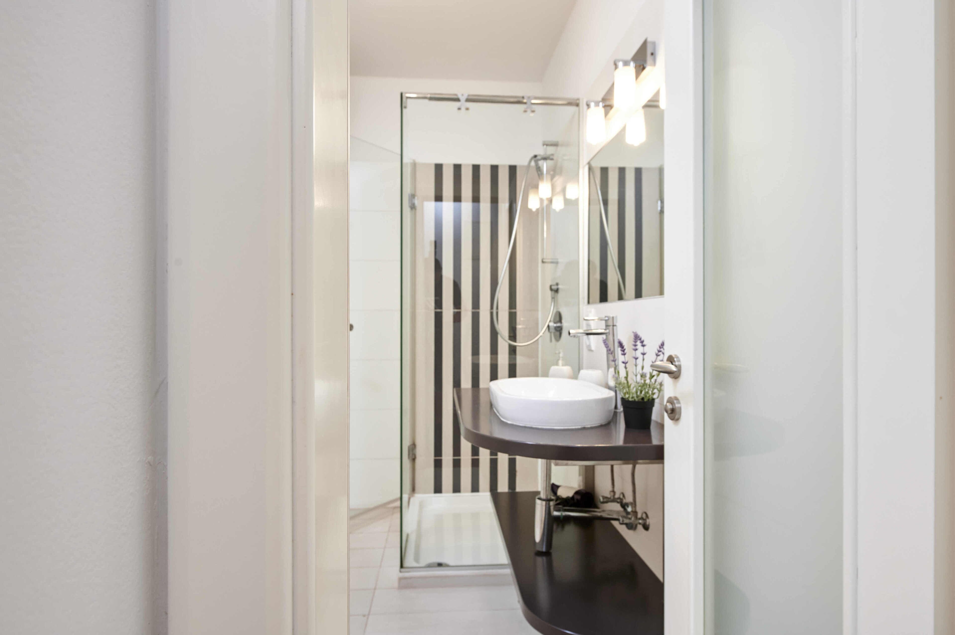 A modern bathroom with a glass shower enclosure, a white sink, and a mirror with lights.