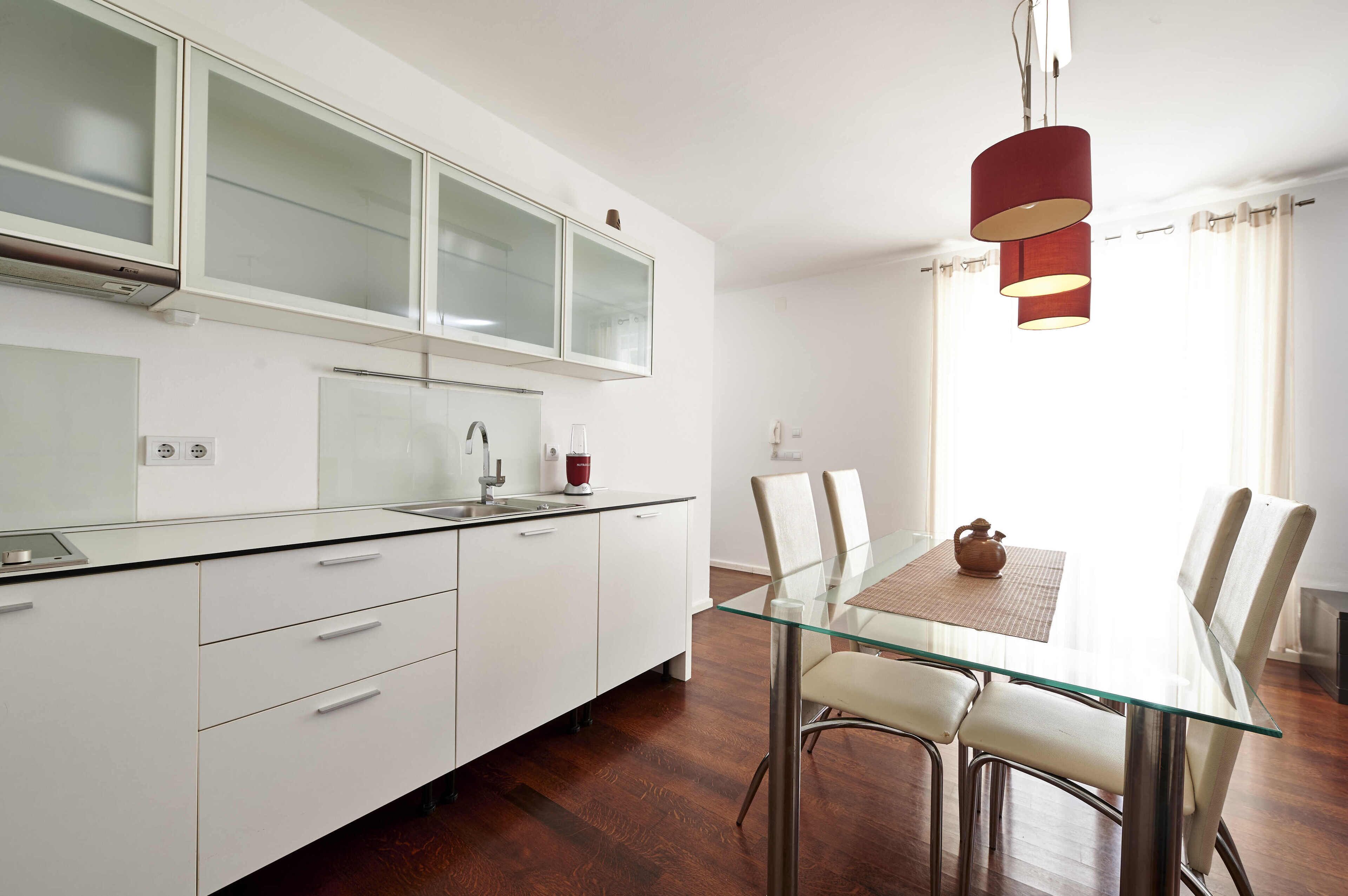 Una cocina moderna con armarios blancos, una mesa de comedor de vidrio y una lámpara colgante roja.