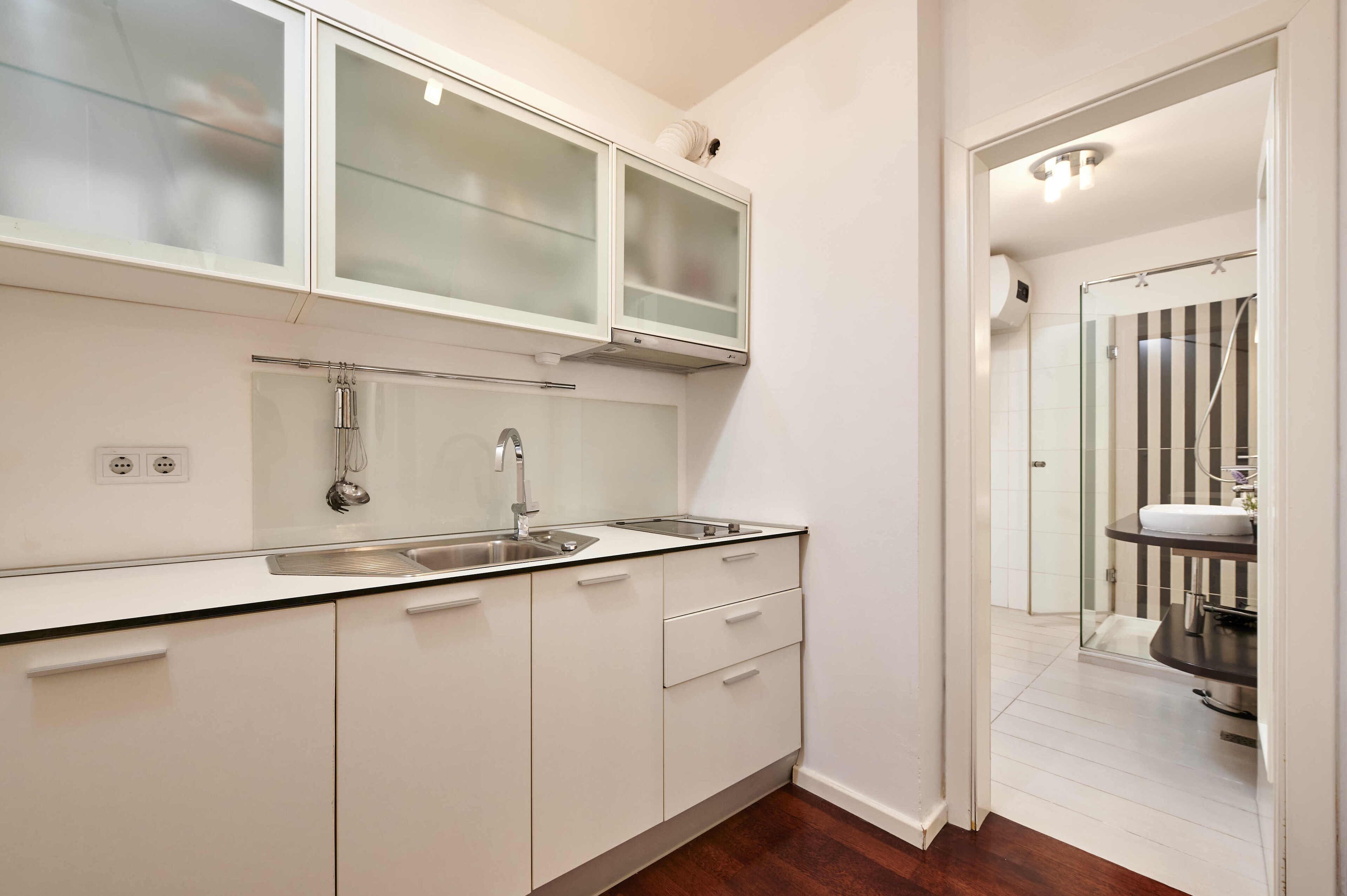 A modern kitchen with white cabinets, a stainless steel sink, and a glass shower enclosure.