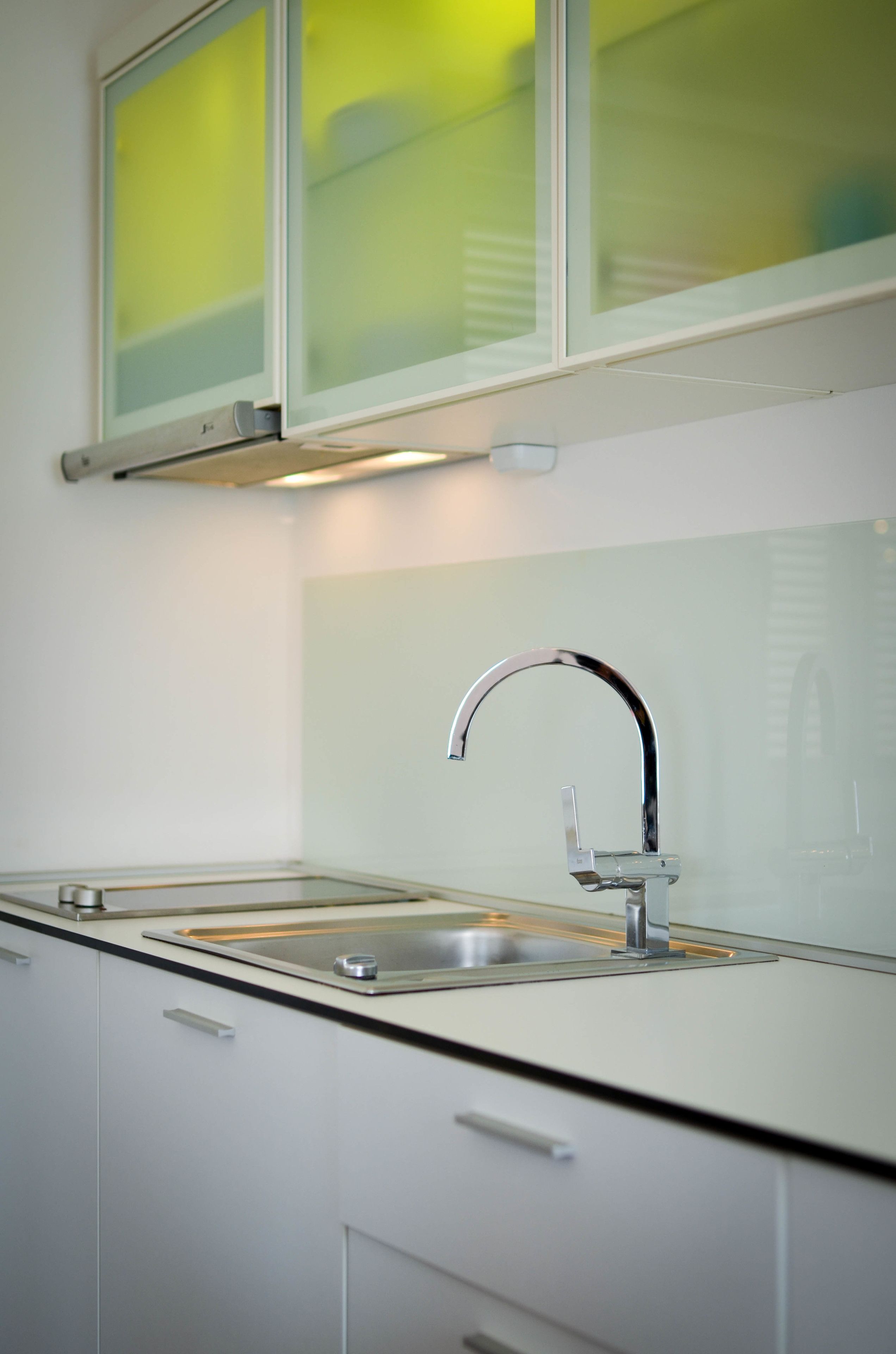 A modern kitchen with a stainless steel sink, white cabinets, and a frosted glass window above the sink.