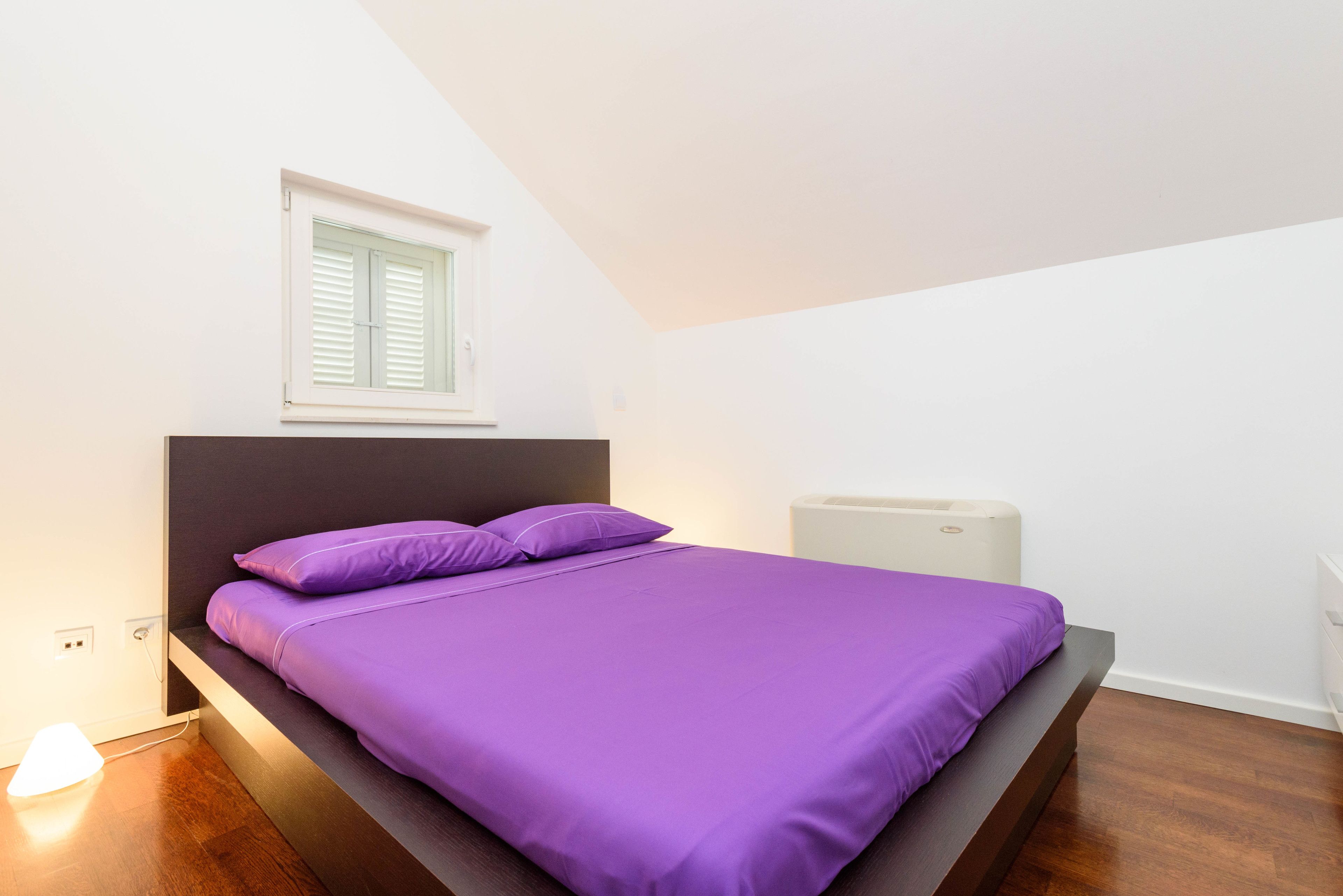 A bedroom with a bed, a window, a bedside table, and a lamp.
