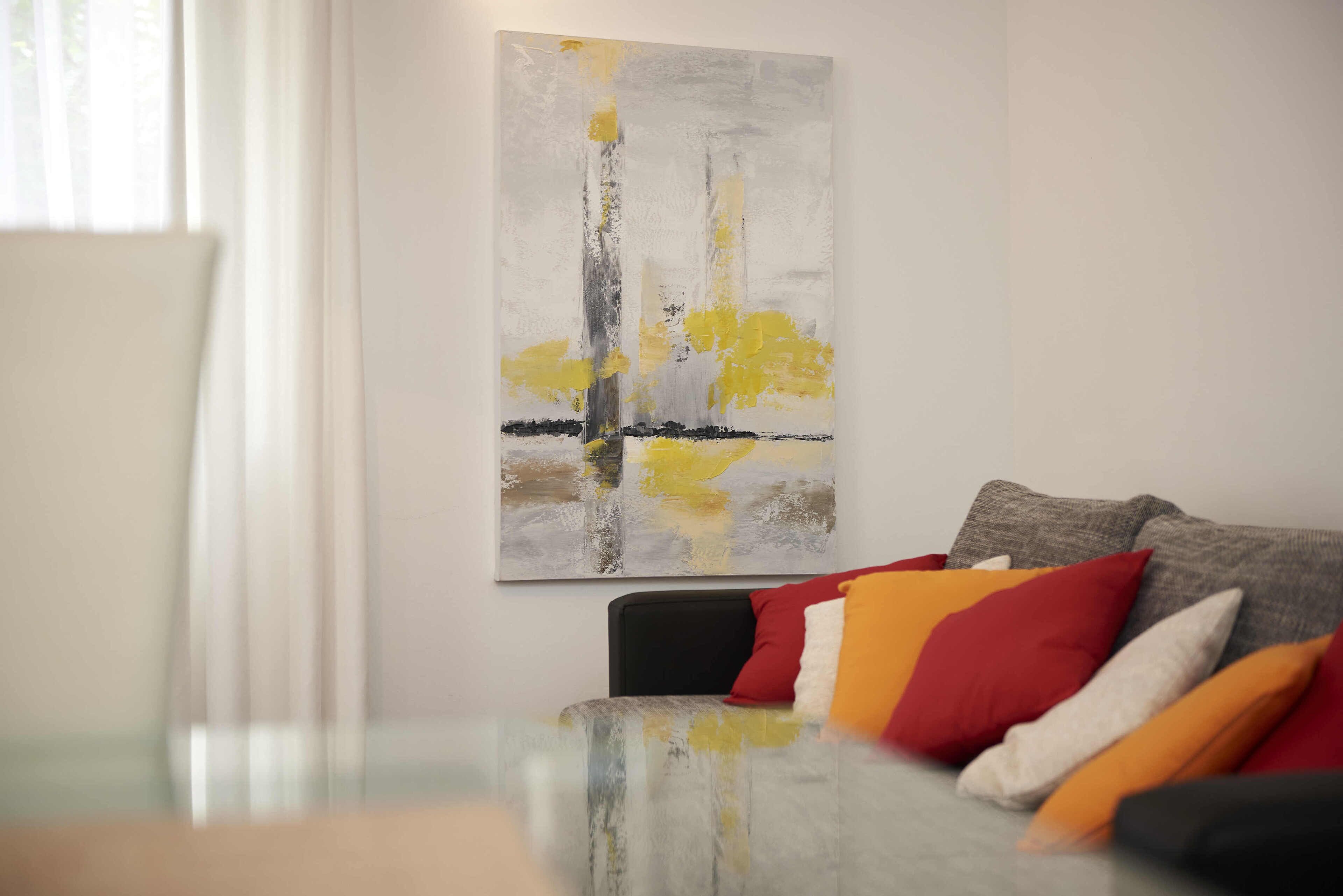 Un salon moderne avec une table basse en verre, un canapé agrémenté de coussins colorés et un grand tableau abstrait accroché au mur.
