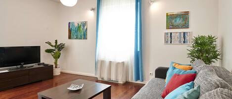 A living room with a sofa, a coffee table, a TV, and a potted plant.