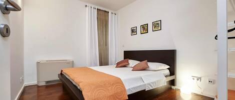 Un dormitorio moderno con suelo de madera, una cama con colcha blanca y naranja, un calentador y una lámpara de pared.