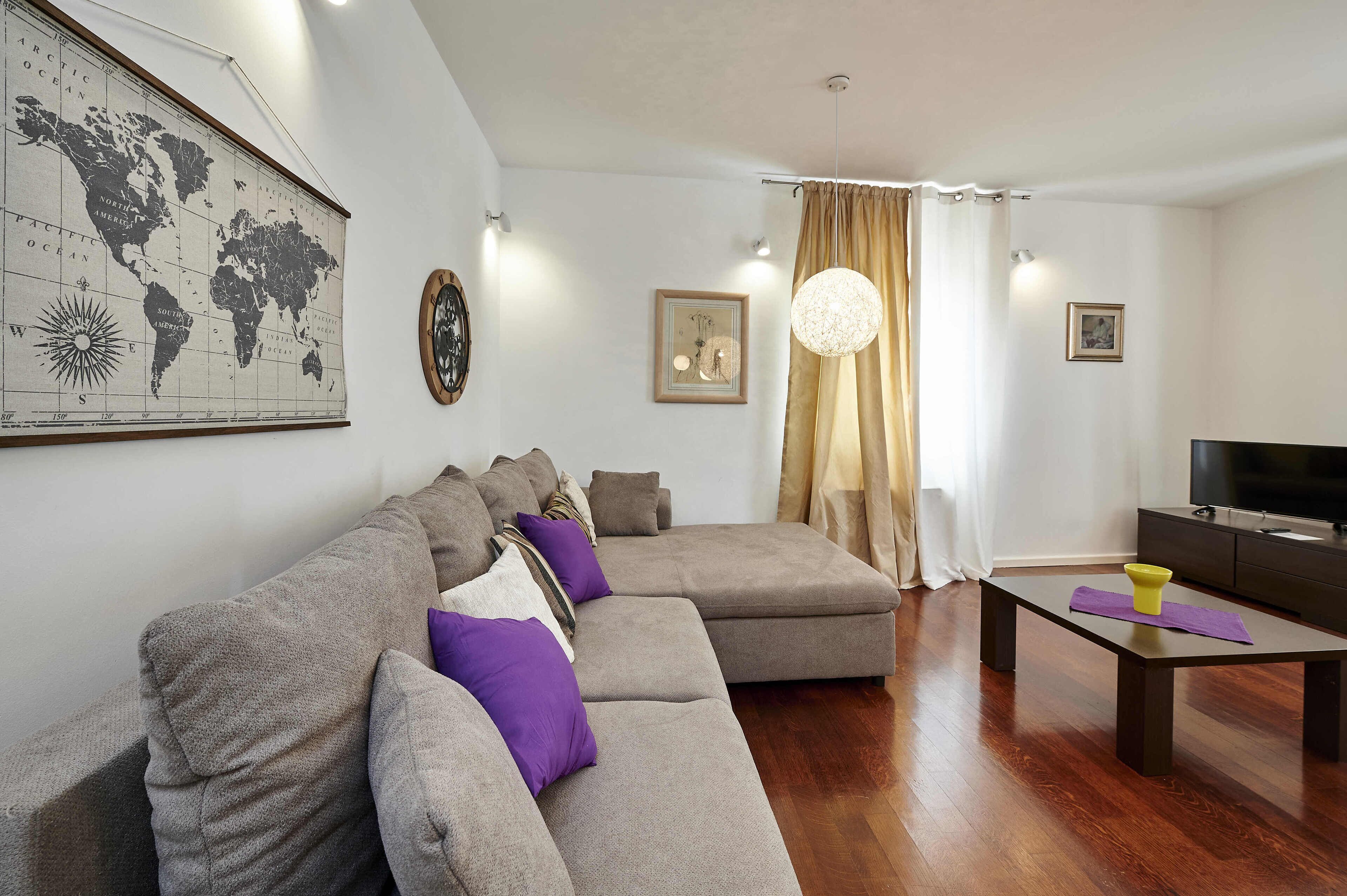 A modern living room with a sectional sofa, a flat-screen TV, a coffee table, and a world map on the wall.