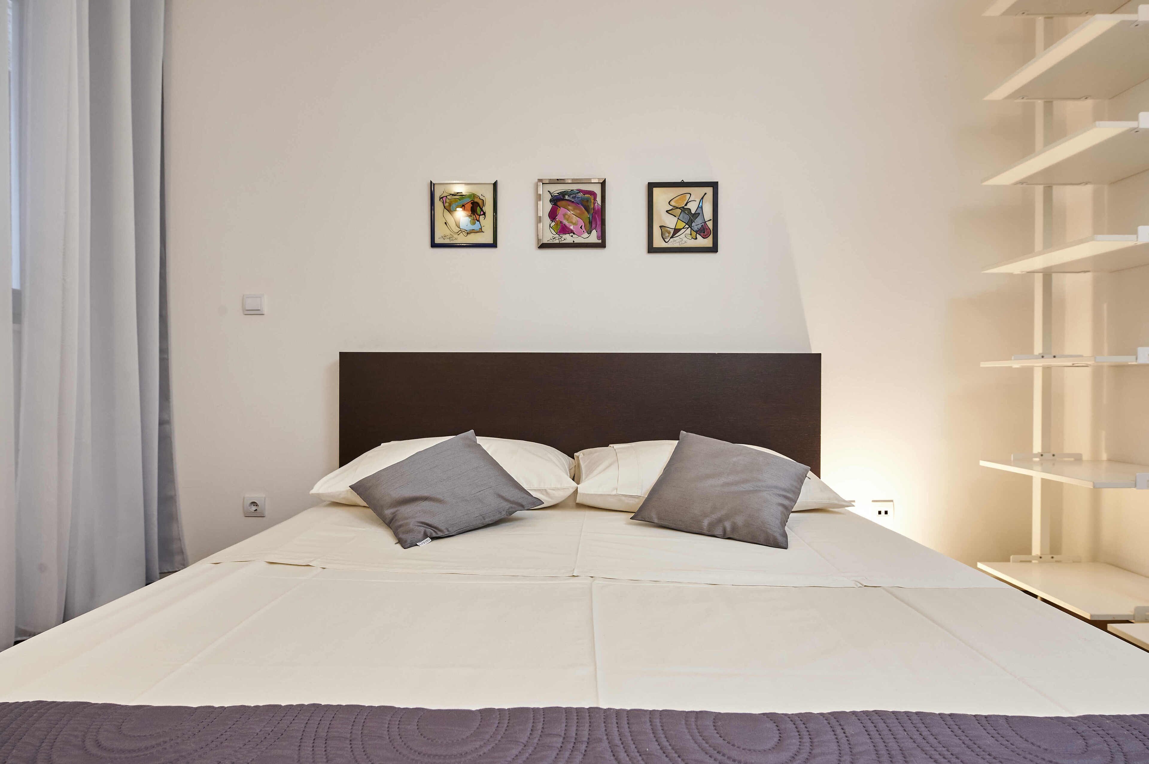 Ein Schlafzimmer mit einem Bett, Kissen und drei gerahmten Kunstwerken an der Wand.