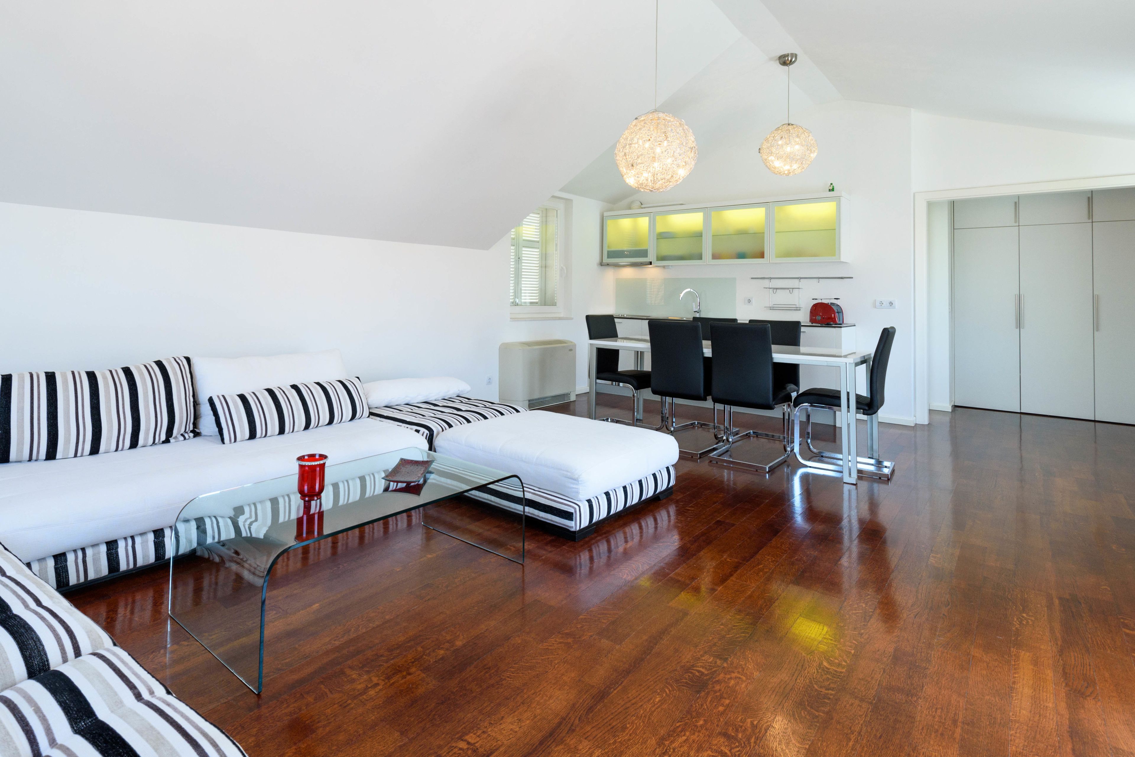 Un salon moderne avec un canapé, une table basse et un coin repas comprenant des chaises, et une cuisine en arrière-plan.