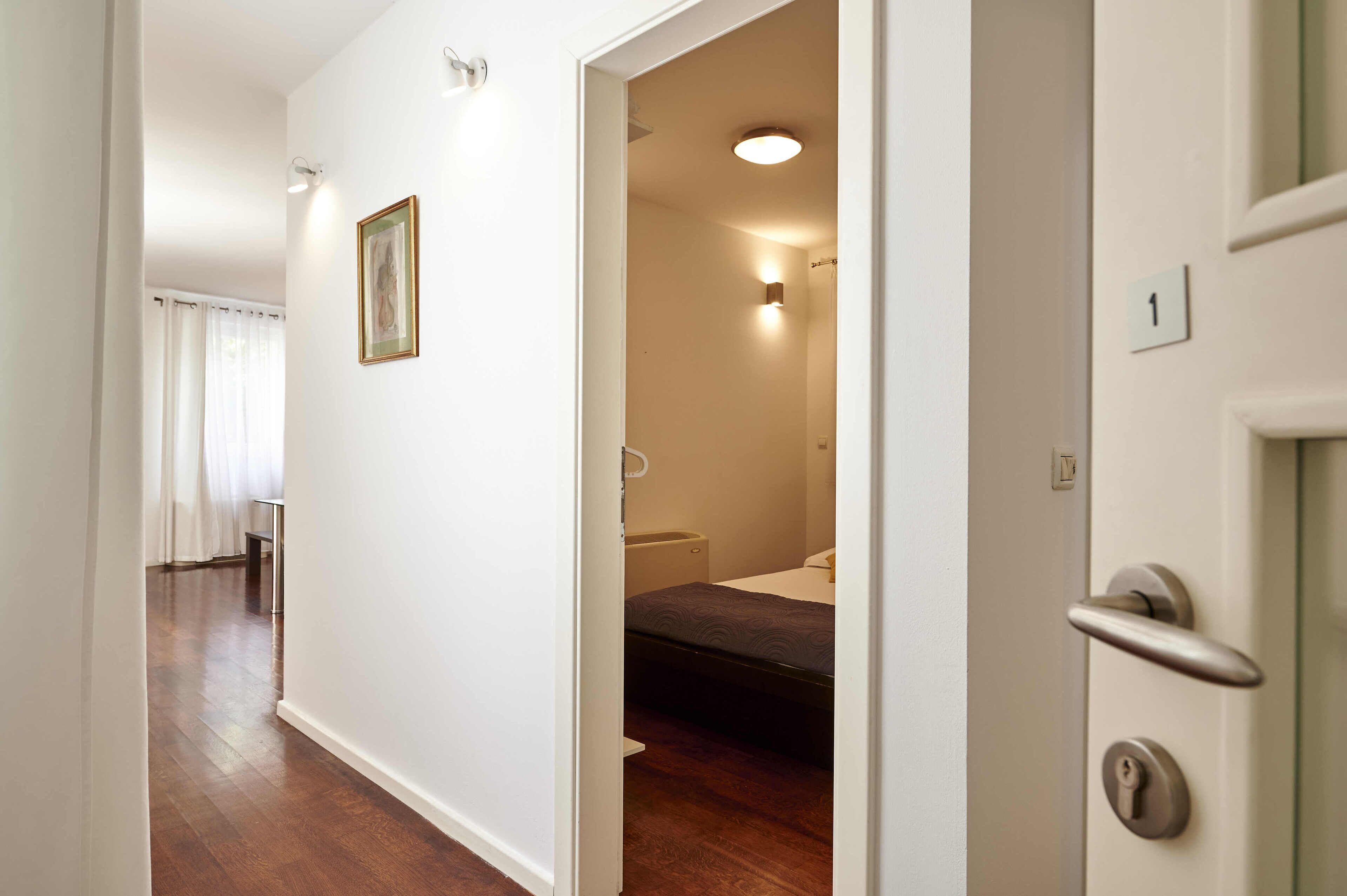 A hallway leading to a bedroom with a bed, a bedside table, and a nightstand.