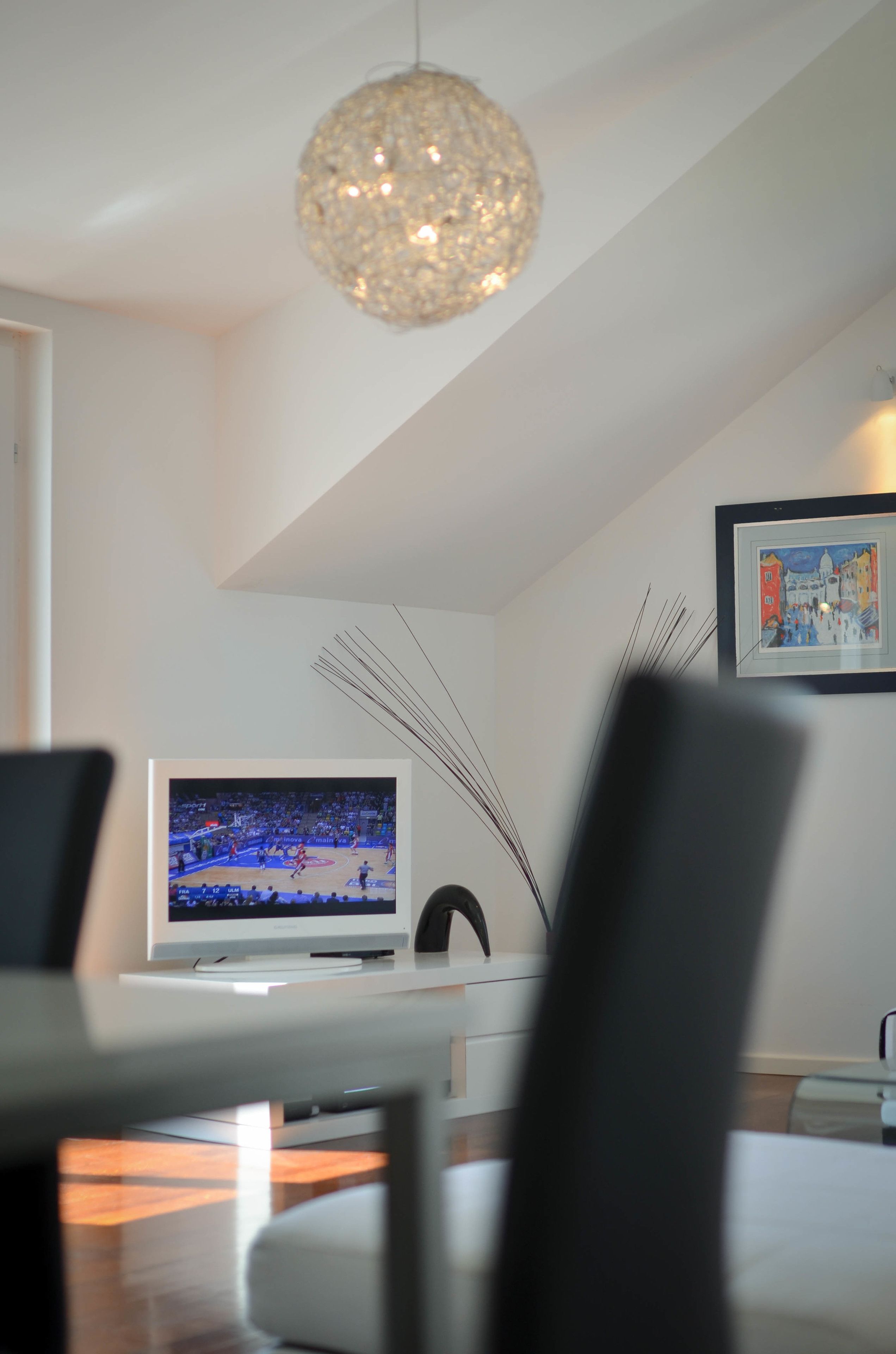 A modern living room with a flat-screen TV, a decorative light fixture, and a framed picture on the wall.