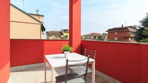 A red balcony with a white table and two chairs, a potted plant, and a view of neighboring houses. - Studio with Balcony Rho Fiera R 10 (RHO)