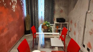 A dining area with red chairs, a white table, and a glass partition. There is a basket with plants on the table, and a shelf with items in the background. - Studio with Balcony Rho Fiera R 10 (RHO)