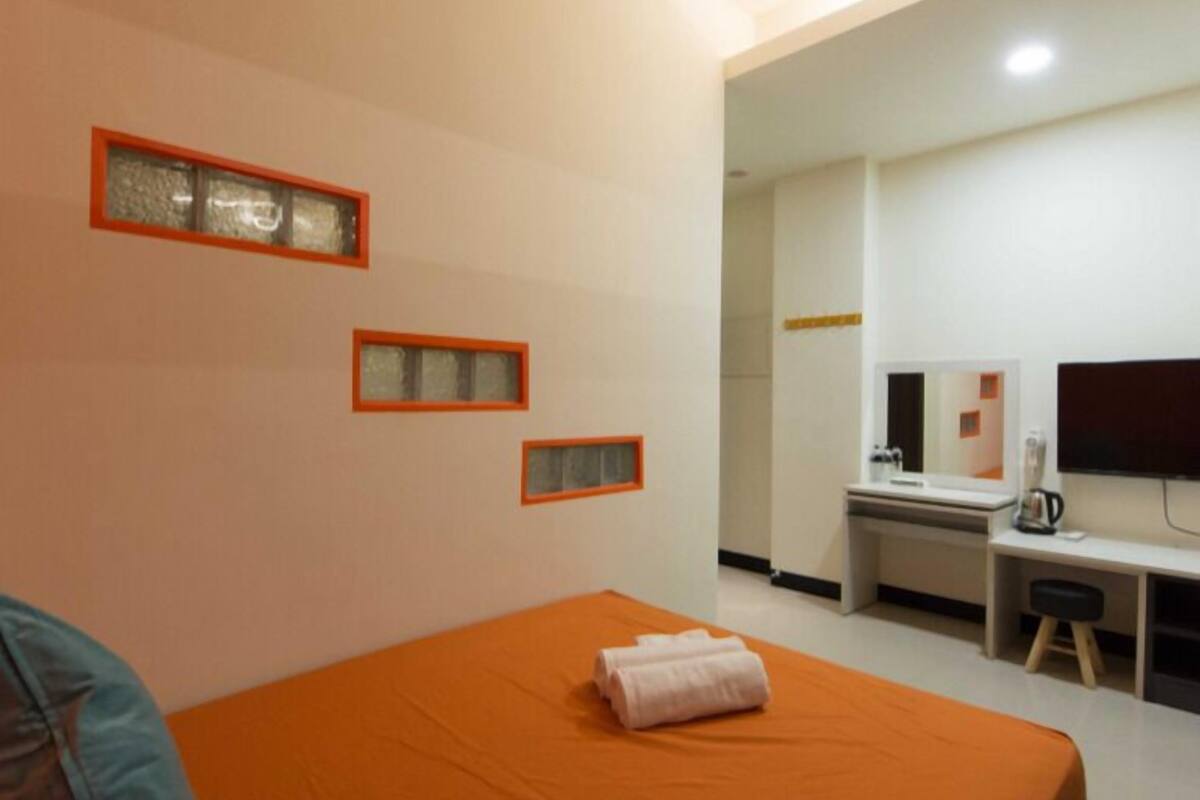 A hotel room with a bed, a desk, a chair, a TV, and a bathroom visible through an open door.