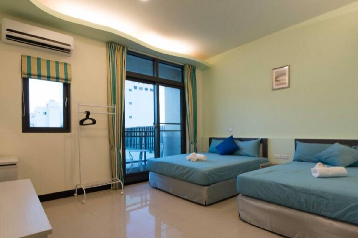 A hotel room with two beds, a desk, and a view of a balcony.