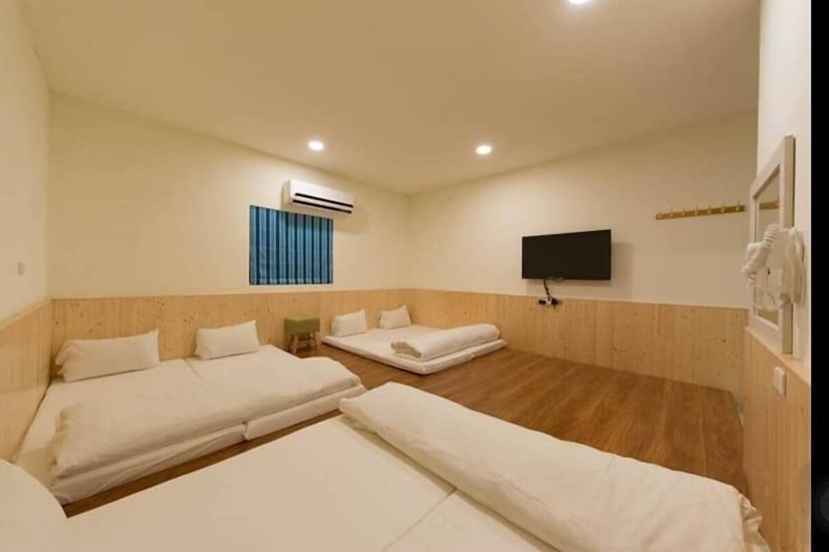 A hotel room with two beds, a flat-screen TV, an air conditioning unit, and a wooden floor.
