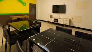 Ein Konferenzraum mit Glastisch, schwarzen Stühlen, einer weißen Decke mit einer Kristallleuchtre, einem Wanddesign in Gelb und Grün sowie einem Flachbildfernseher und einem kleinen weißen Schrank.