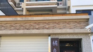 Ein modernes Gebäude mit einer geschlossenen Garagentür, einem Holzzaun und einem Schild mit japanischen Schriftzeichen.