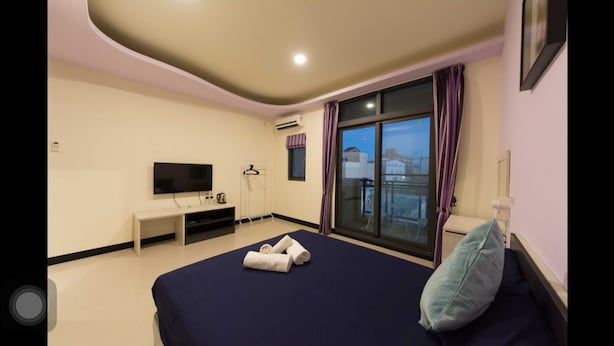 Ein Hotelzimmer mit Bett, Fernseher, Schreibtisch und einem Fenster mit Vorhängen.