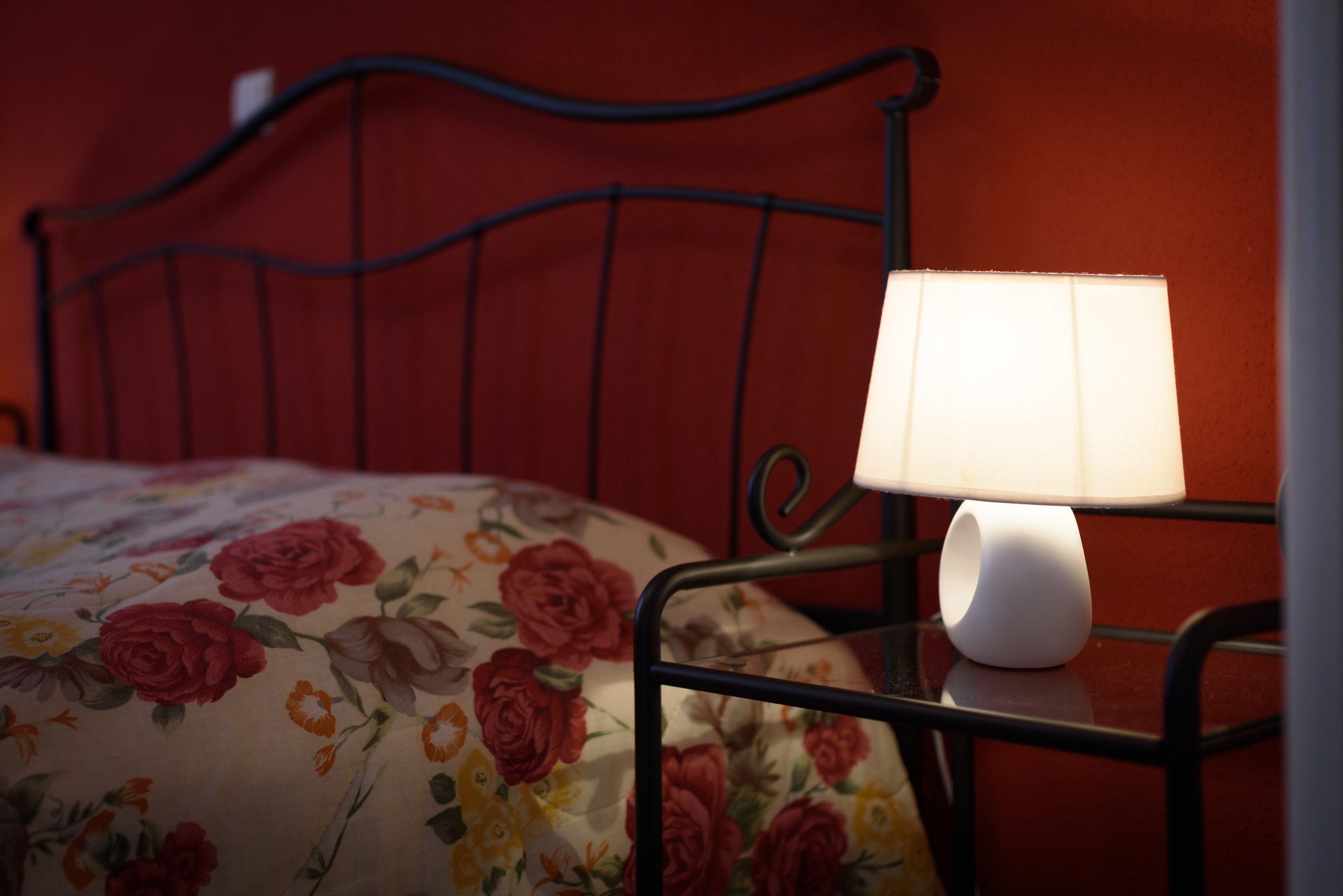 A bed with a floral-patterned bedspread and a white bedside lamp on a metal frame.