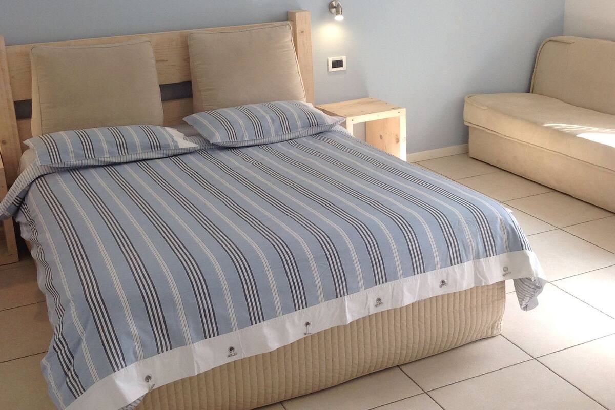 A bedroom with a bed, a nightstand, a wall-mounted light, and a sofa.