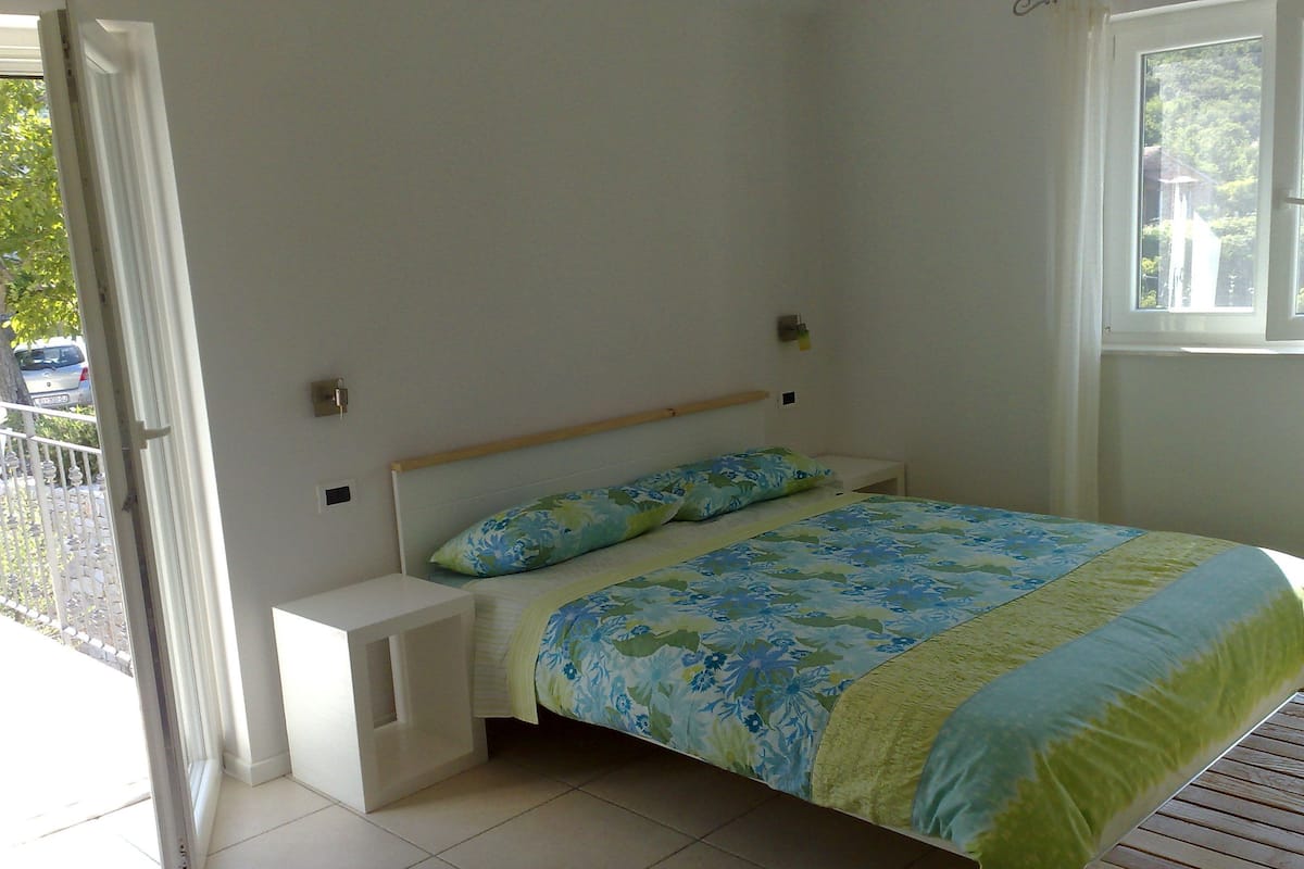 A bedroom with a bed, a nightstand, a window, and a door.